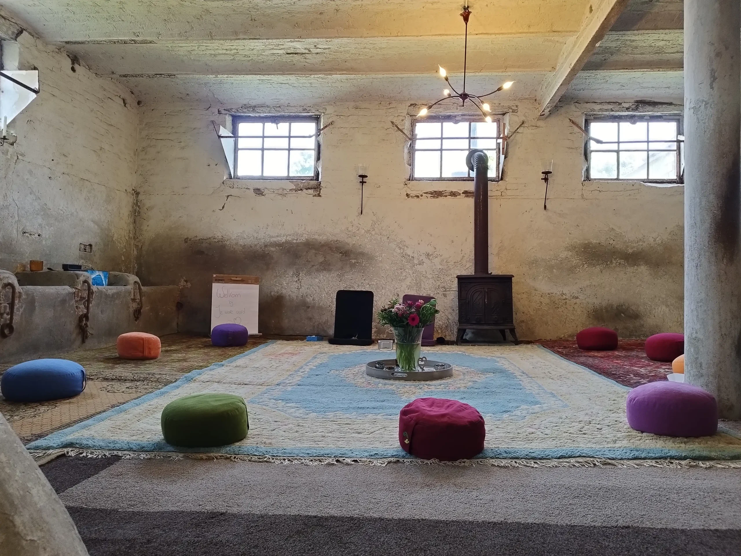 Koeienstal ingericht met meditatiekussens in kring en houtkachel